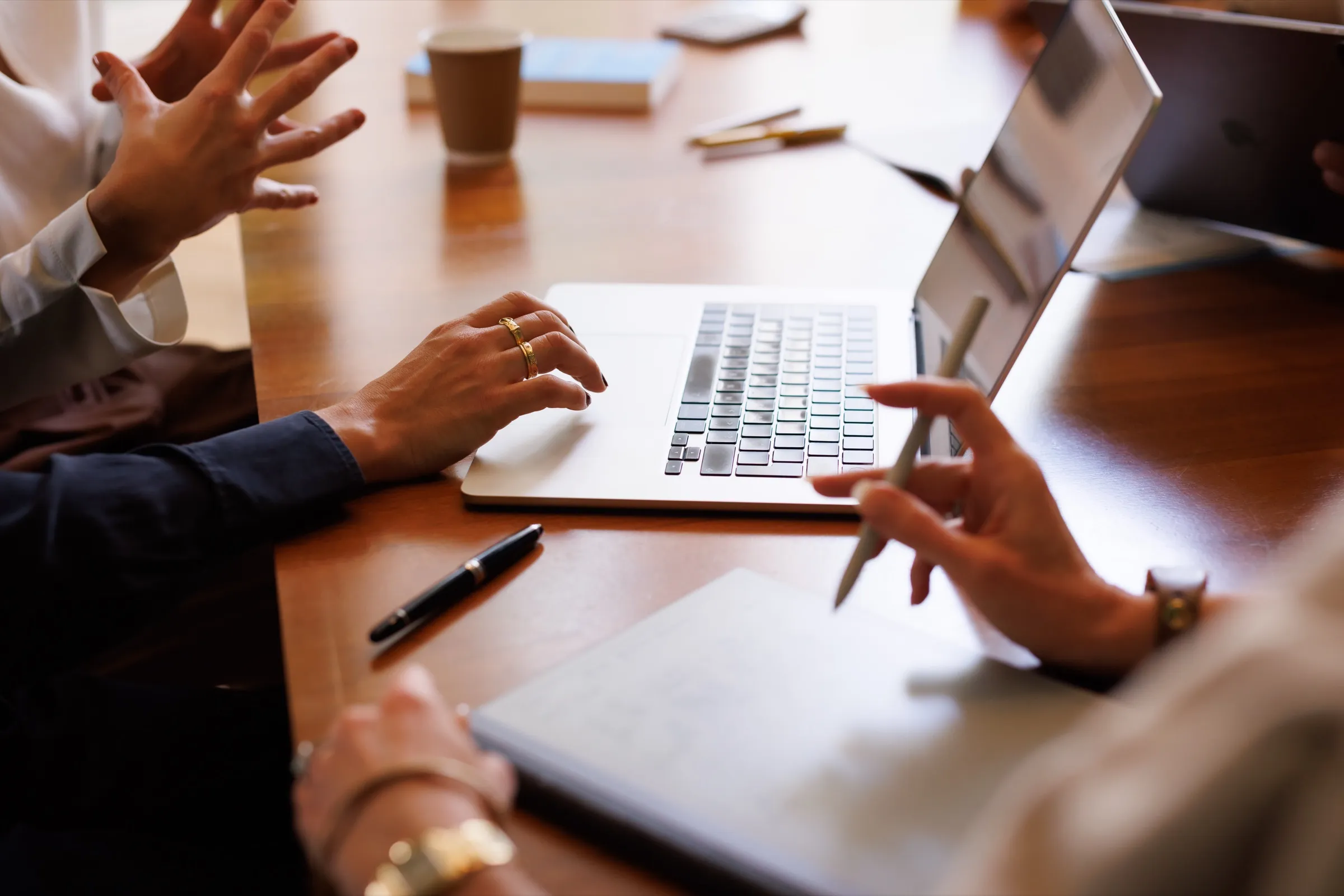 Hands working on a laptop and notepad with documents on a meeting table
