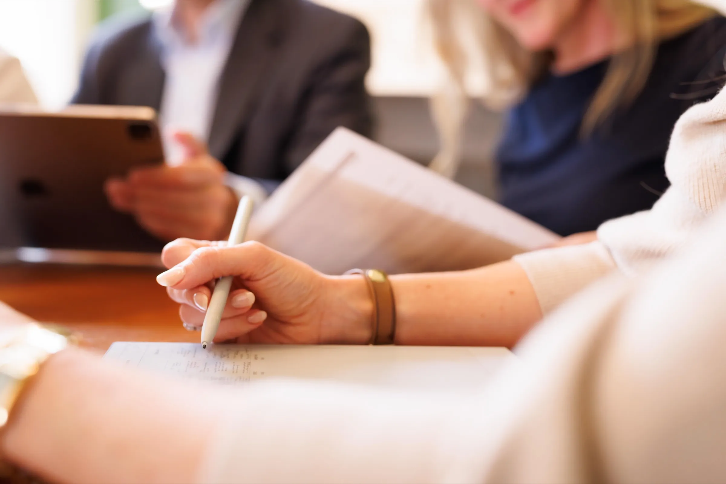 Hand taking notes with a pen during a meeting, papers and a tablet on the table