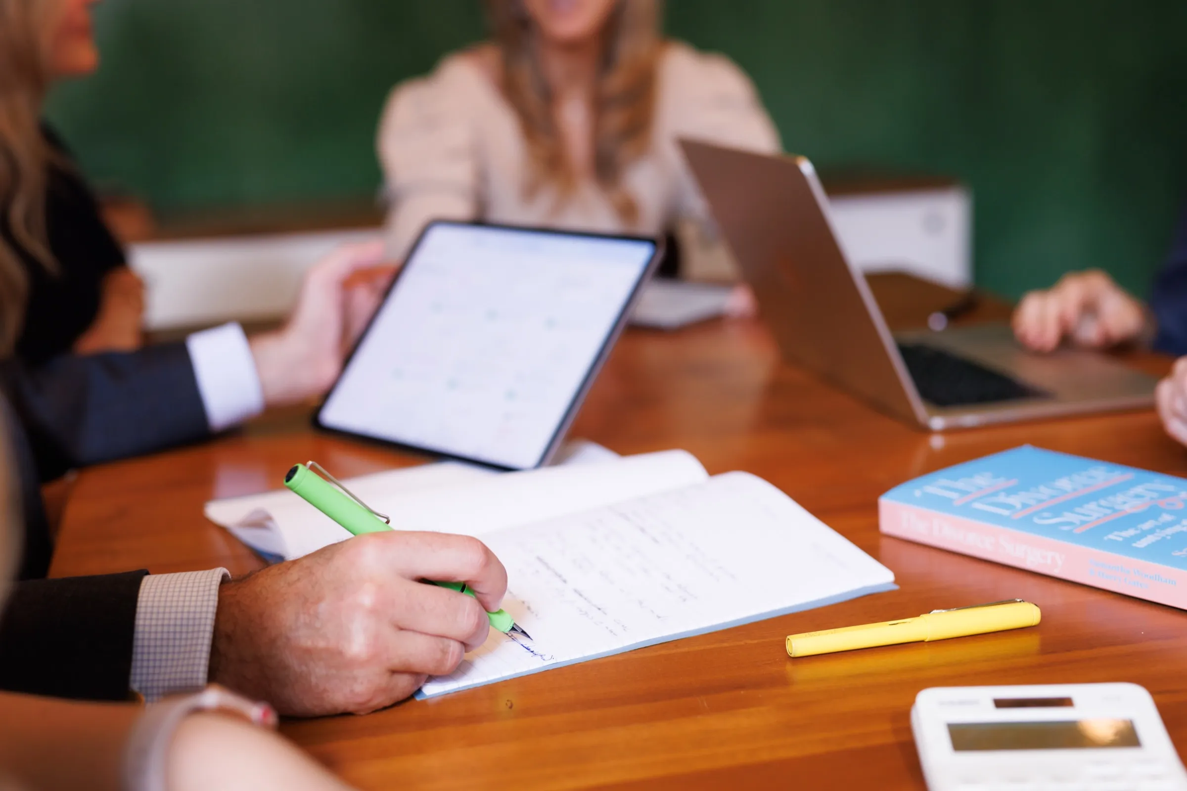 Hand writing detailed notes with a green pen during a meeting